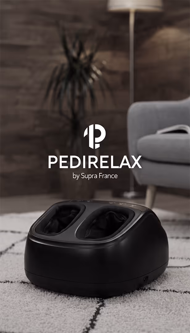 Appareil de massage pour pieds noir Pedirelax posé sur un tapis à motifs dans un salon cosy.