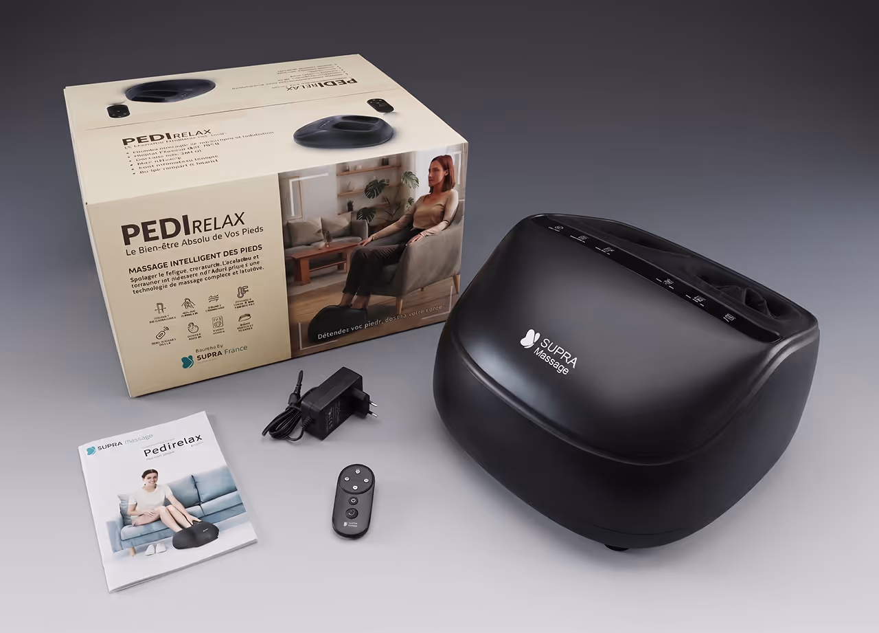 Appareil de massage pour pieds noir SUPRA Massage avec télécommande, transformateur et manuel à côté de sa boîte.