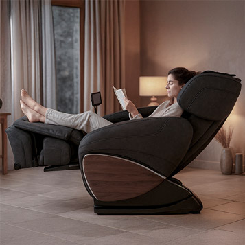 Femme détendue dans un fauteuil massant Évasion 3D, en position relax avec repose-pieds relevé, lisant dans une ambiance chaleureuse.