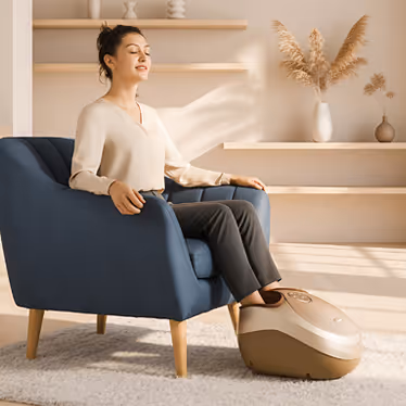 Femme assise dans un fauteuil bleu utilisant l’appareil de massage des pieds FOOTBOX pour un moment de relaxation à la maison