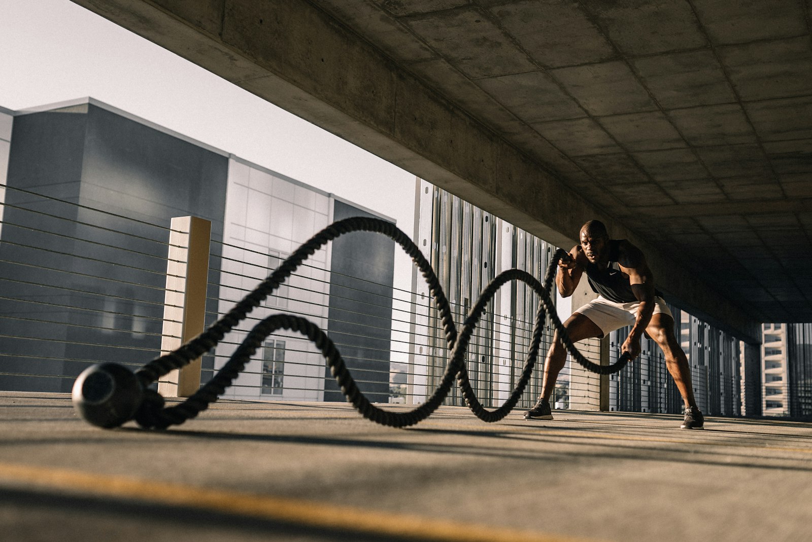 Hombre entrenando con battle ropes al aire libre bajo un aparcamiento