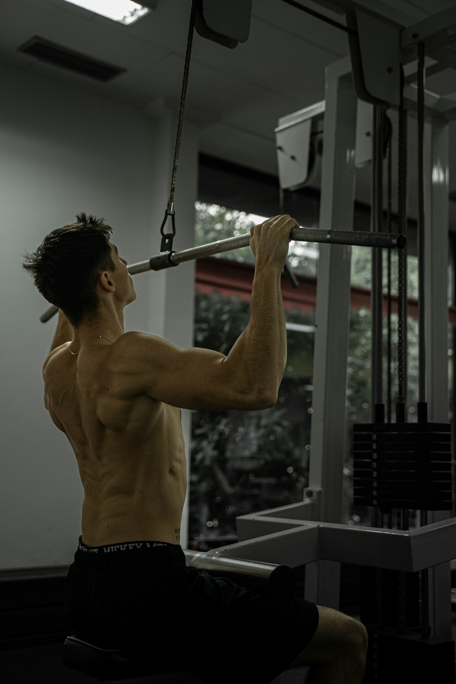 Hombre sentado en la polea alta tirando de la barra hacia el pecho en un gimnasio