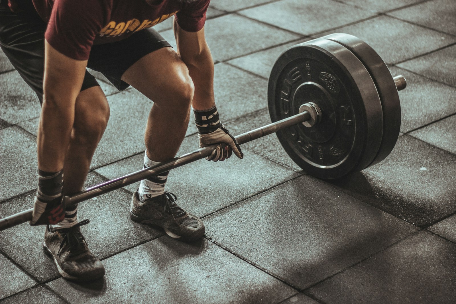 Hombre agarrando una barra cargada con discos en el suelo de un gimnasio