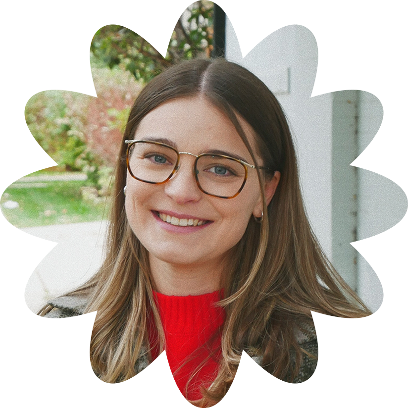 Caroline smiling, wearing glasses and a red top, with a green outdoor background