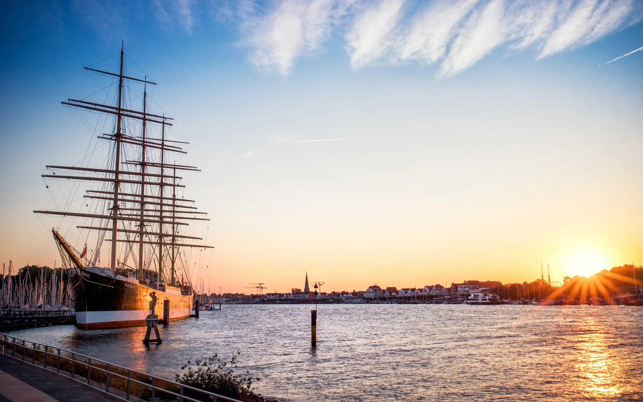 Segelschiff Passat im Hafen von Lübeck bei Sonnenuntergang mit Ufer und Stadt im Hintergrund.