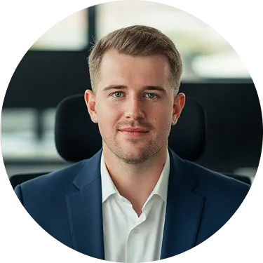 Junger Mann mit kurzem Haar und blauem Sakko vor unscharfem Bürohintergrund.