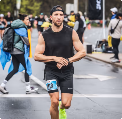 Male runner in black sleeveless shirt and shorts with race bib 1913 checking watch during a road race.