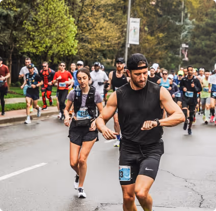 Runners participating in an outdoor race on a tree-lined street, with one man checking his watch in the foreground.