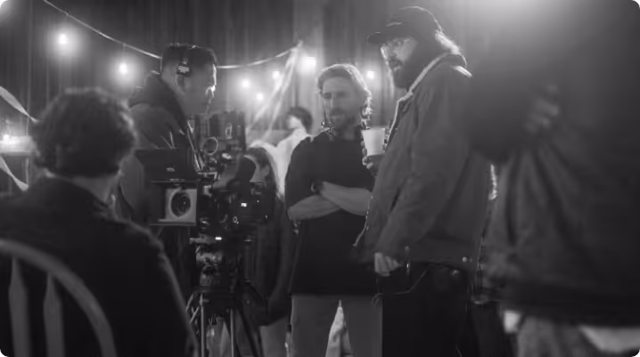 Film crew working on set with camera equipment and string lights in the background.