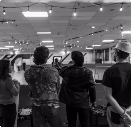 Four people standing indoors, one recording with a camera, surrounded by string lights on the ceiling.
