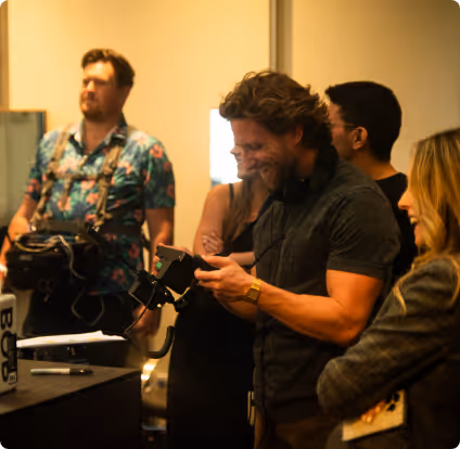 Group of people engaged in conversation and checking a device in a warmly lit indoor setting.