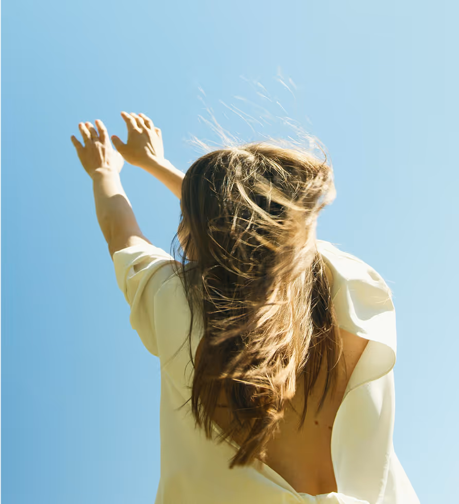 Person with arms raised against blue sky