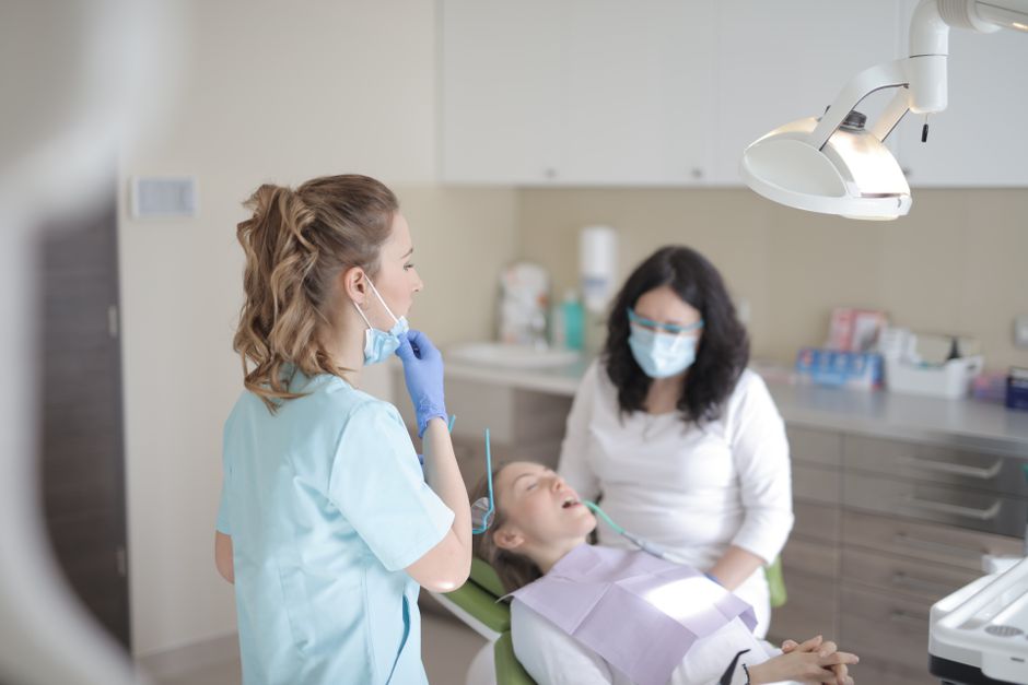 Smiling young child sitting in dental chair during first dentist visit with friendly dentist nearby.