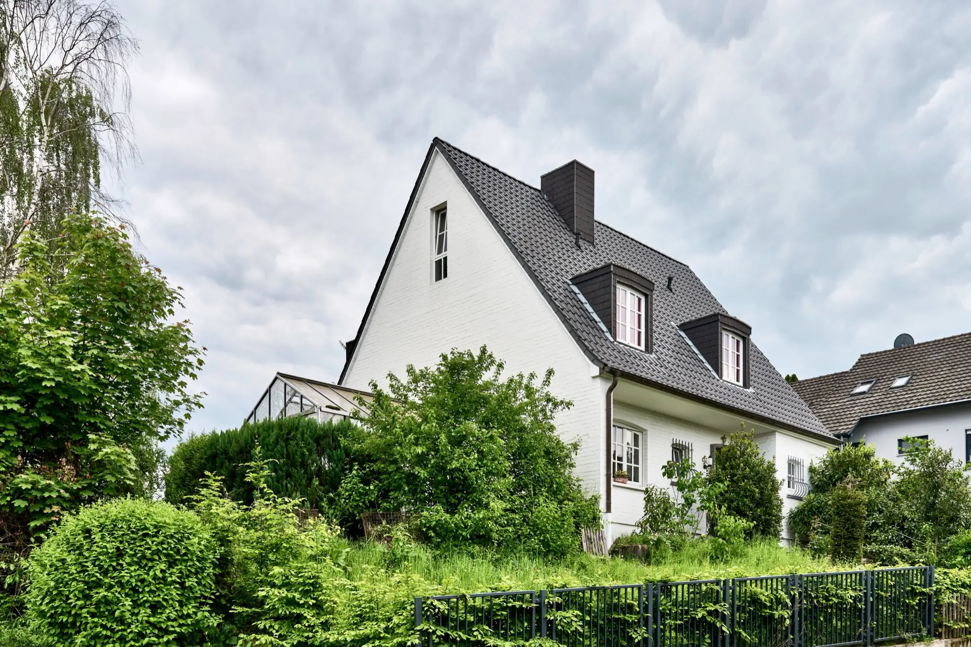 Außenansicht des weißen Einfamilienhauses mit dunklem Dach und Wintergarten in Bonn-Duisdorf