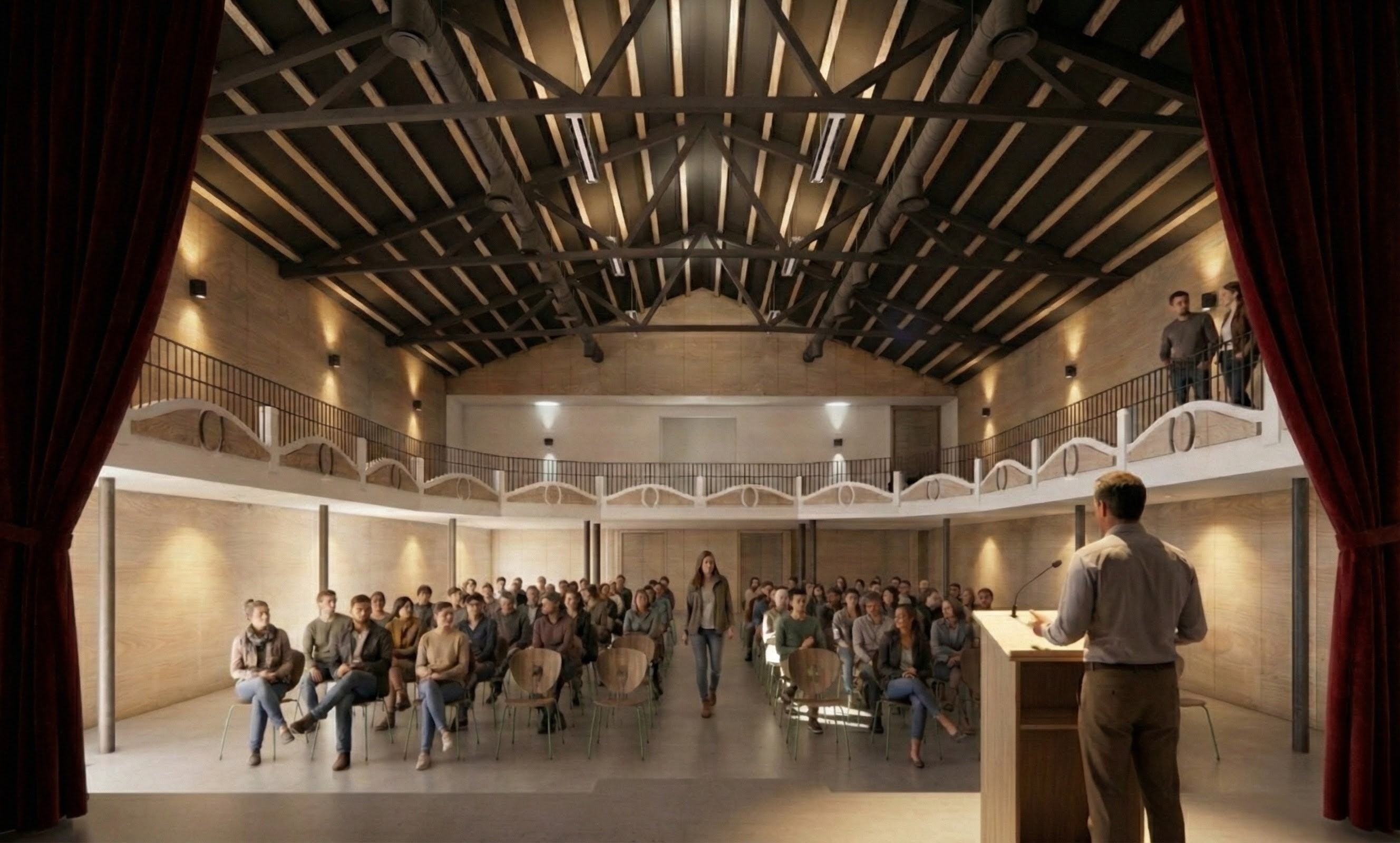 Man speaking at a podium to an audience seated in rows inside a modern theater with exposed wooden beams and balcony seating.