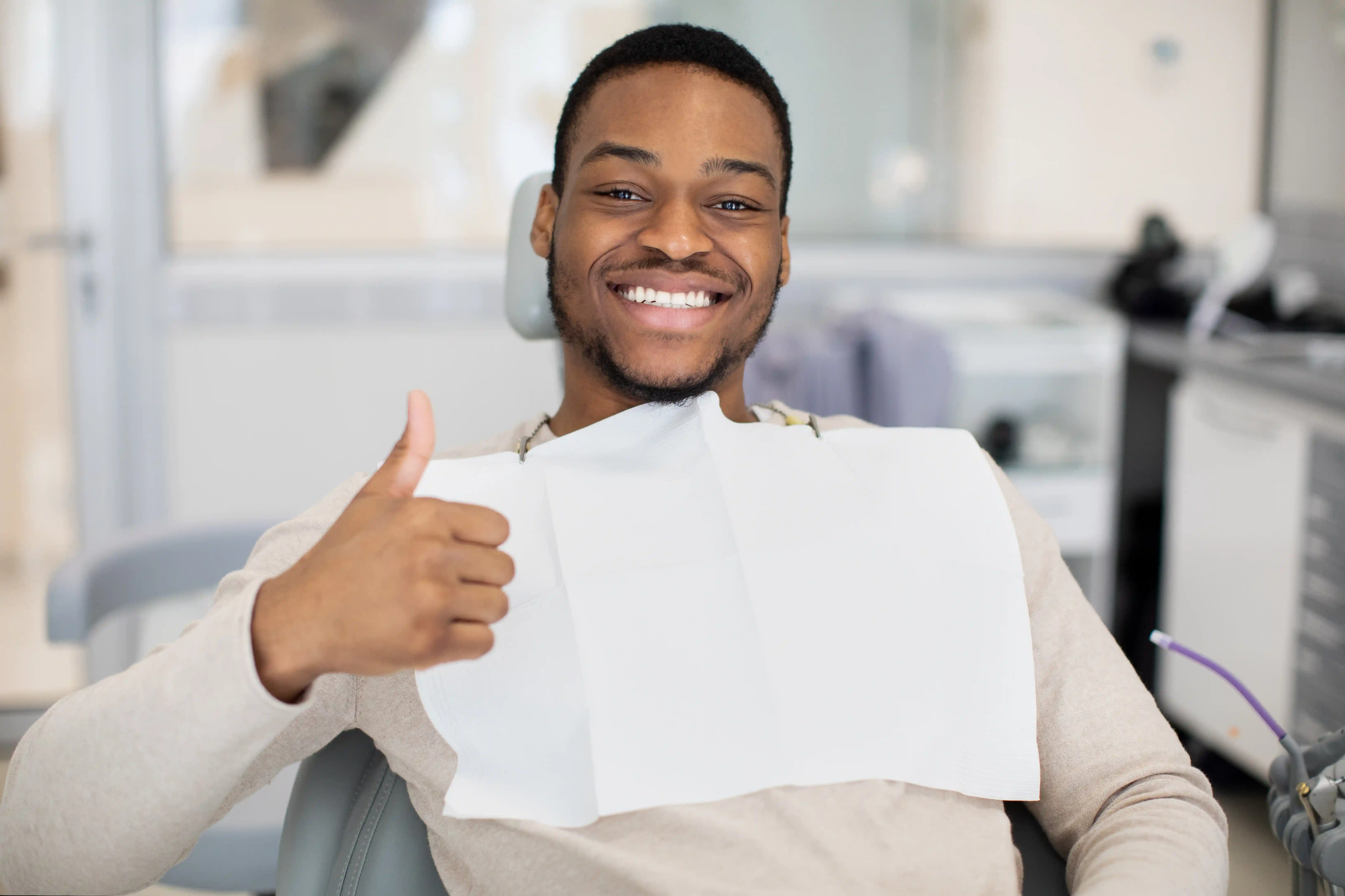 Smiling man sitting in a dental chair wearing a bib and giving a thumbs up.