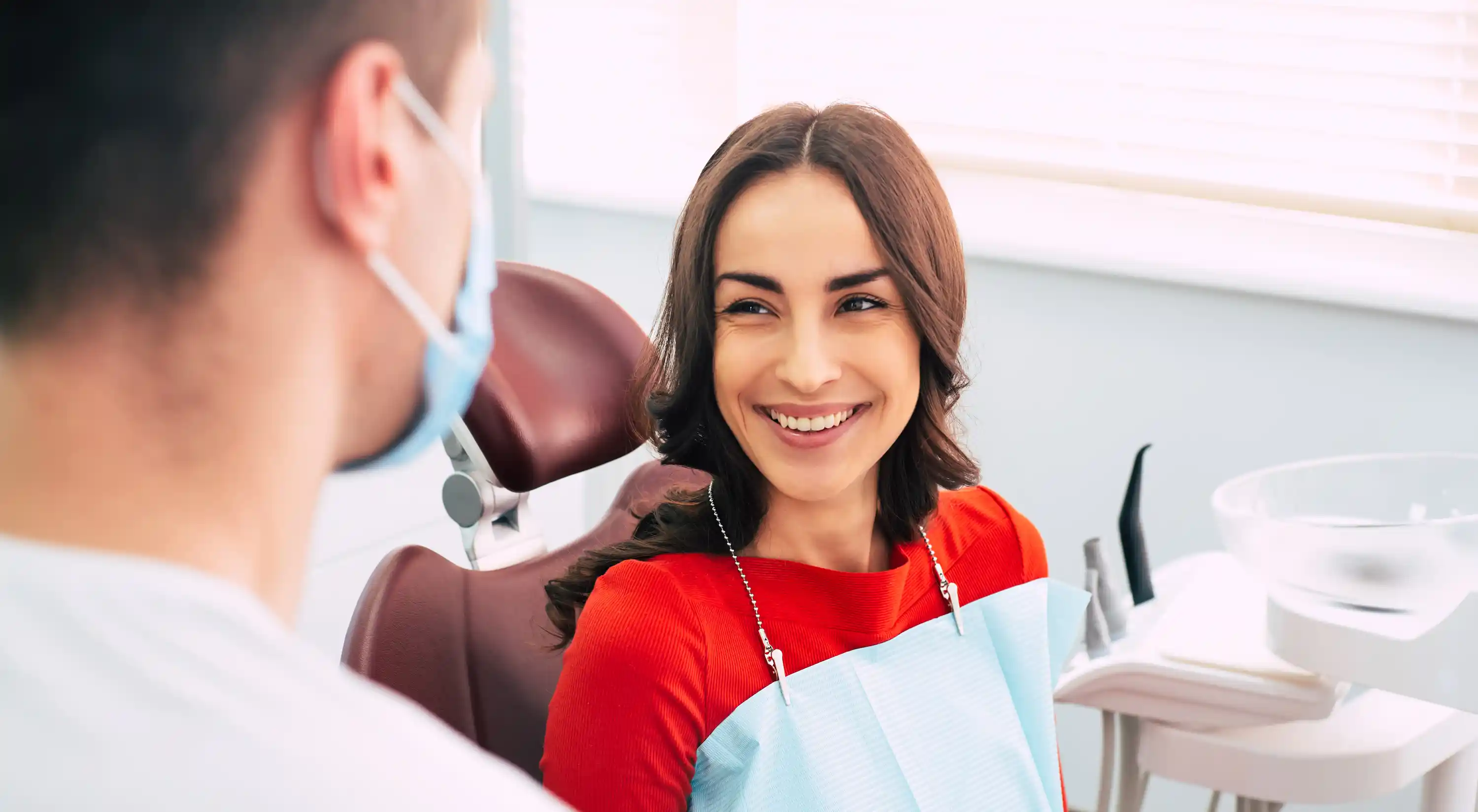 Smiling woman in a dental chair looking at a masked dentist.