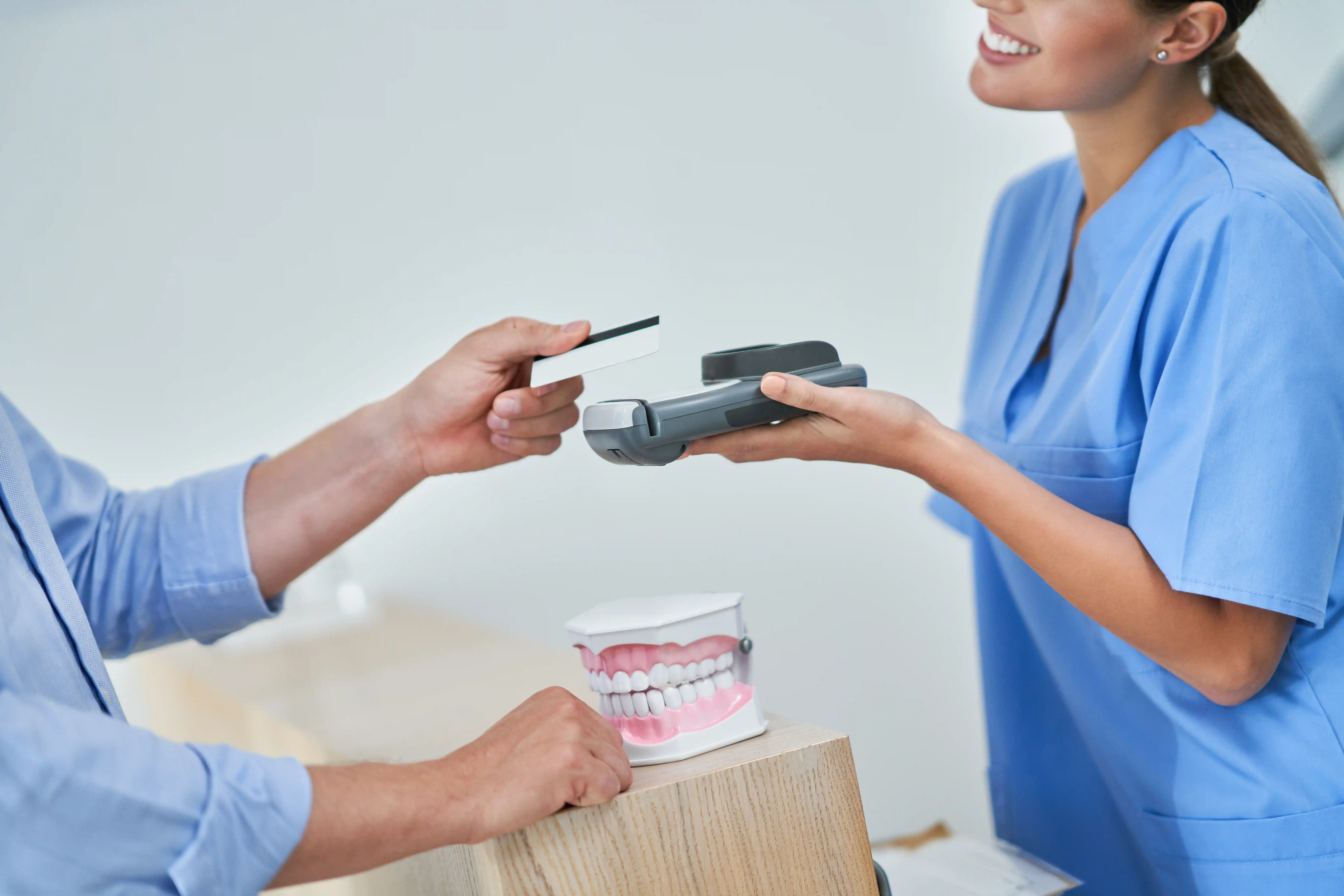 A woman in blue scrubs holding a payment terminal as a person swipes a credit card.