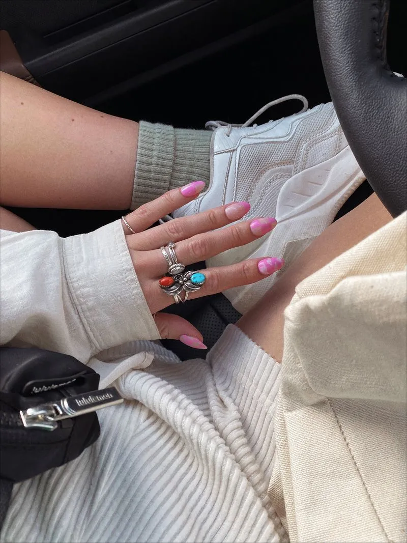 Hand with pink swirl nails and rings in car