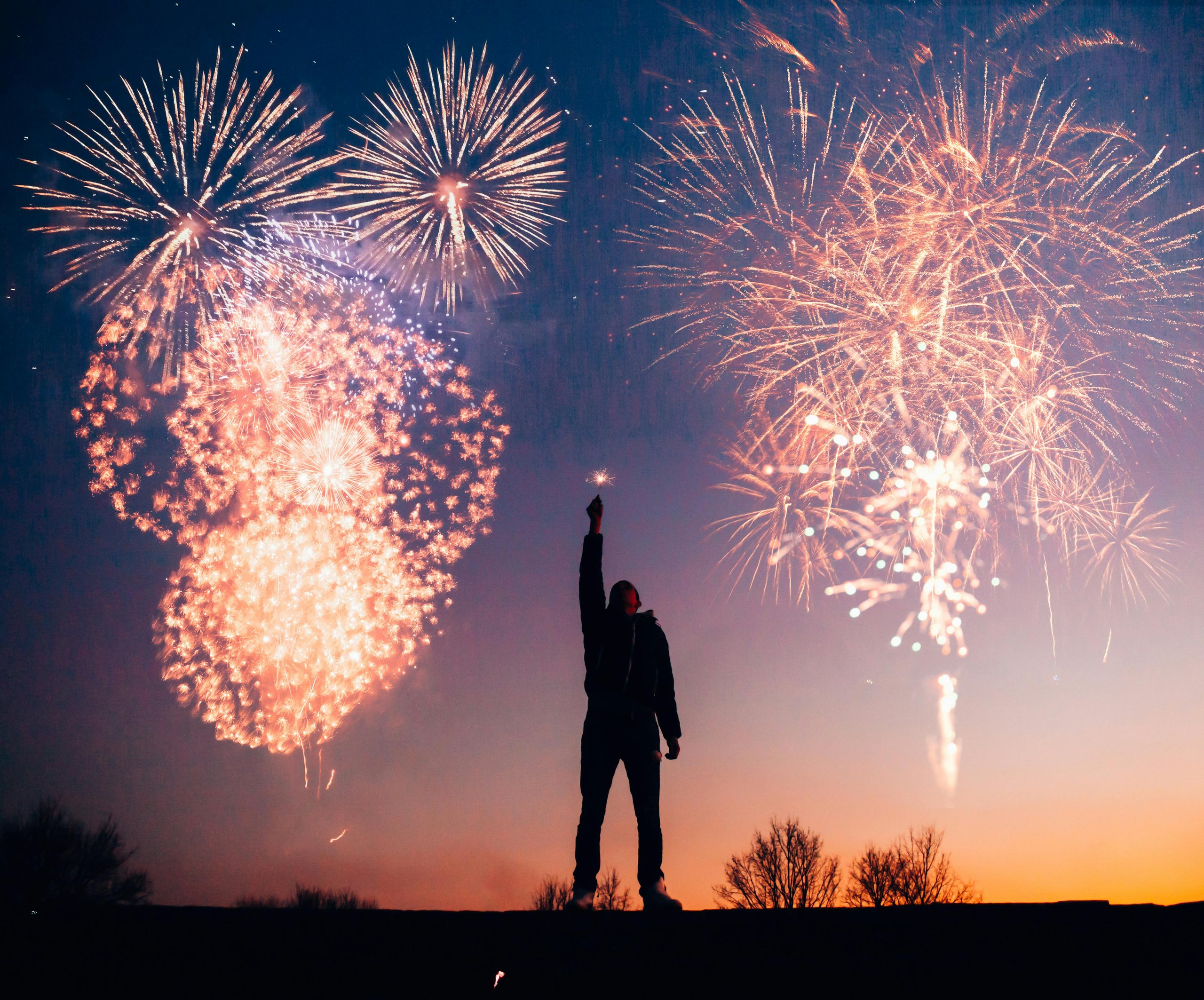 A man holding a light up in his hand with fireworks in the background