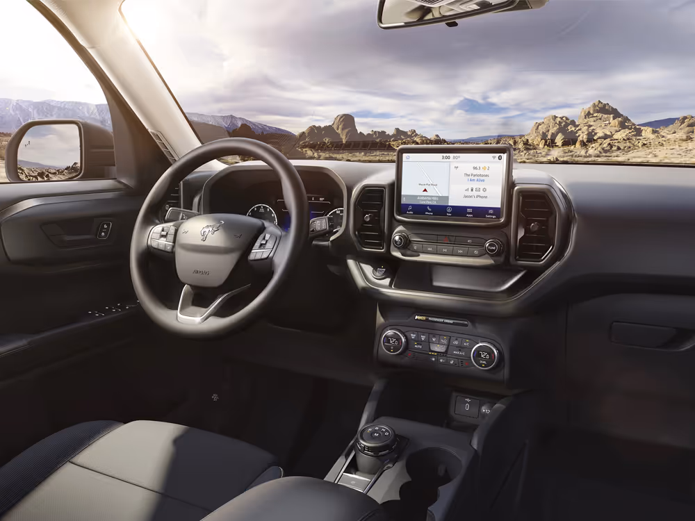 Interior view of Ford Bronco Sport with digital display and desert landscape through windshield, commercial automotive photography.