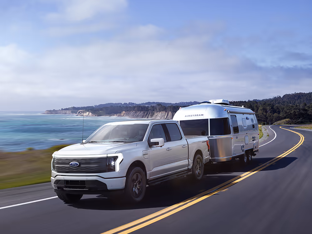White Ford F-150 towing silver Airstream trailer along ocean highway, commercial automotive travel photography by Roe Photo.