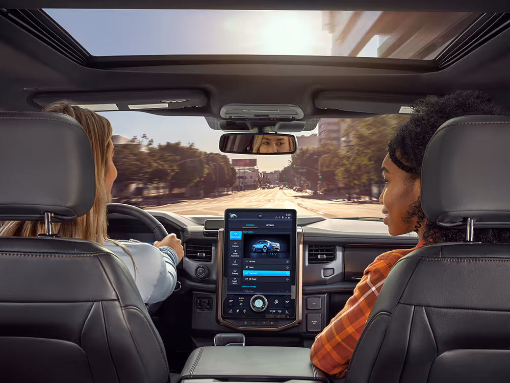 Two women driving through city streets, modern automotive lifestyle photography with digital dashboard display by Roe Photo.