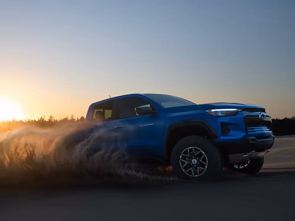 Blue pickup truck driving over sand dune at golden hour, desert automotive photo shoot by Roe Photo.