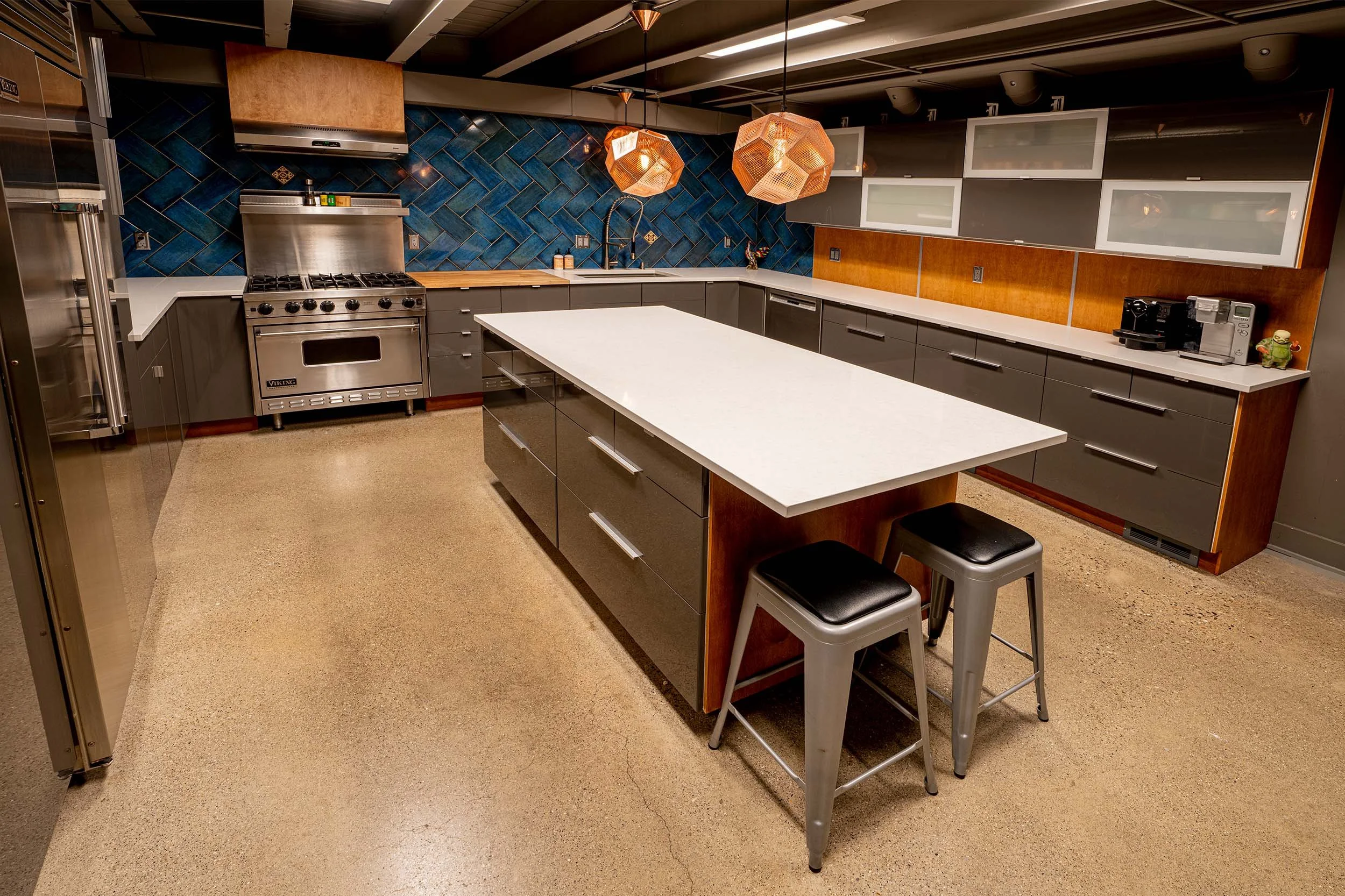 Studio kitchen with professional-grade Viking range, blue tile backsplash, modern pendant lights, and polished concrete floors.