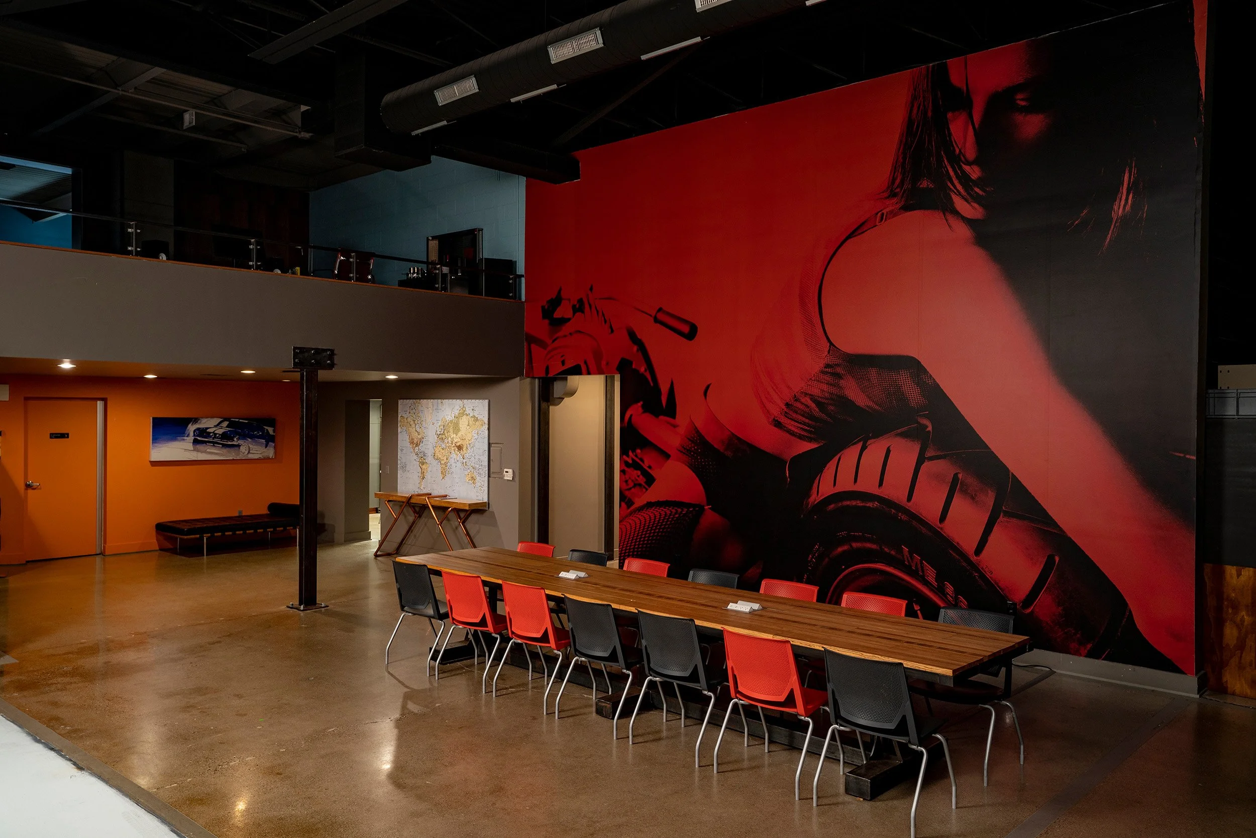Detroit studio conference space with long wooden meeting table, red and black chairs, polished concrete floors, and large red wall mural of woman and motorcycle tire.