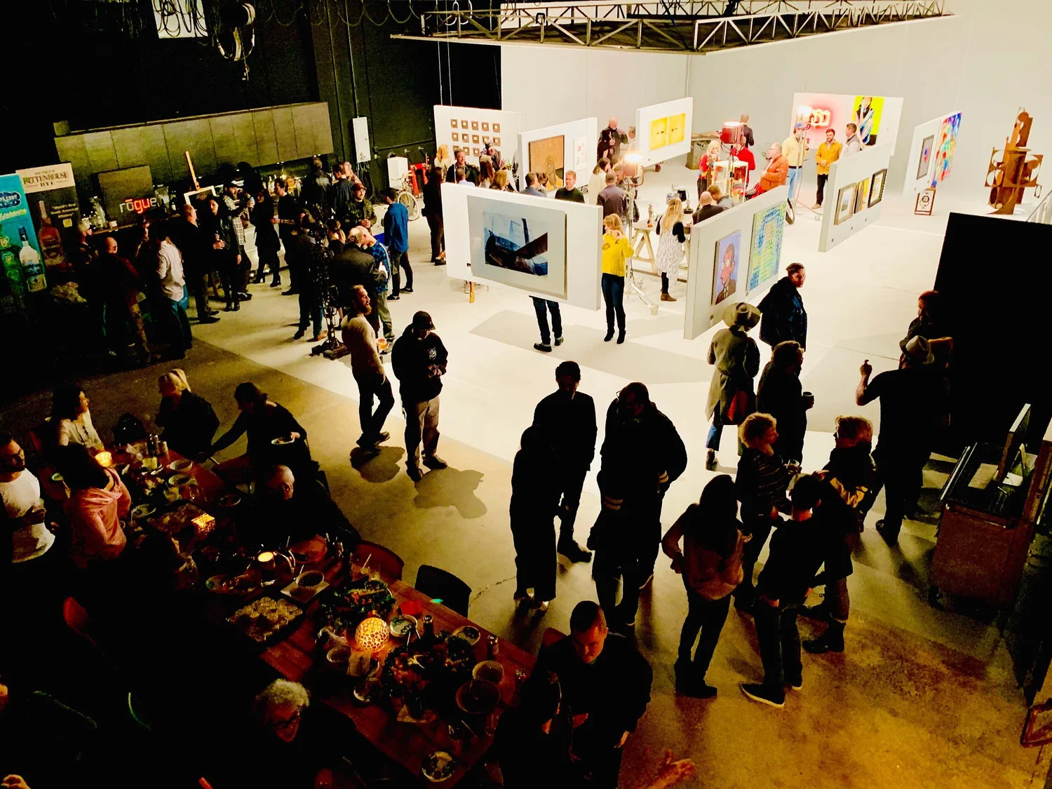 Creative industry event hosted in Detroit production studio, guests mingling and viewing art installations under studio lighting.