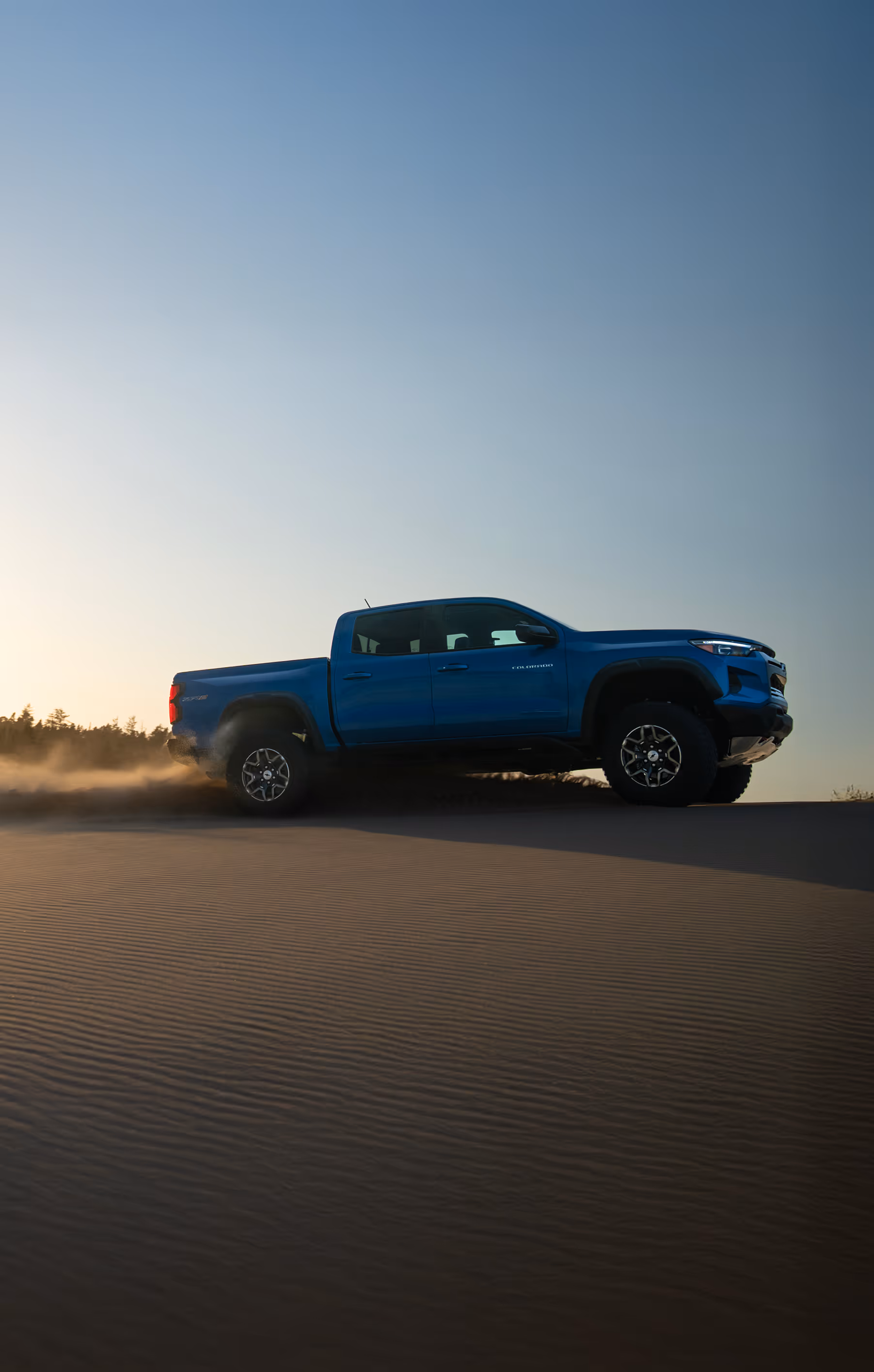Blue pickup truck driving over sand dune at golden hour, desert automotive photo shoot by Roe Photo.