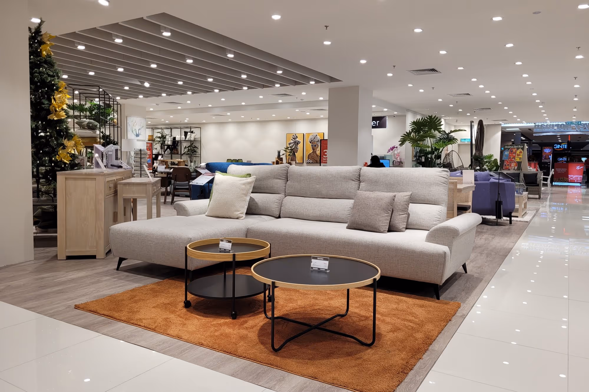 Modern furniture showroom featuring a light gray sectional sofa on an orange rug with two round black coffee tables in front.