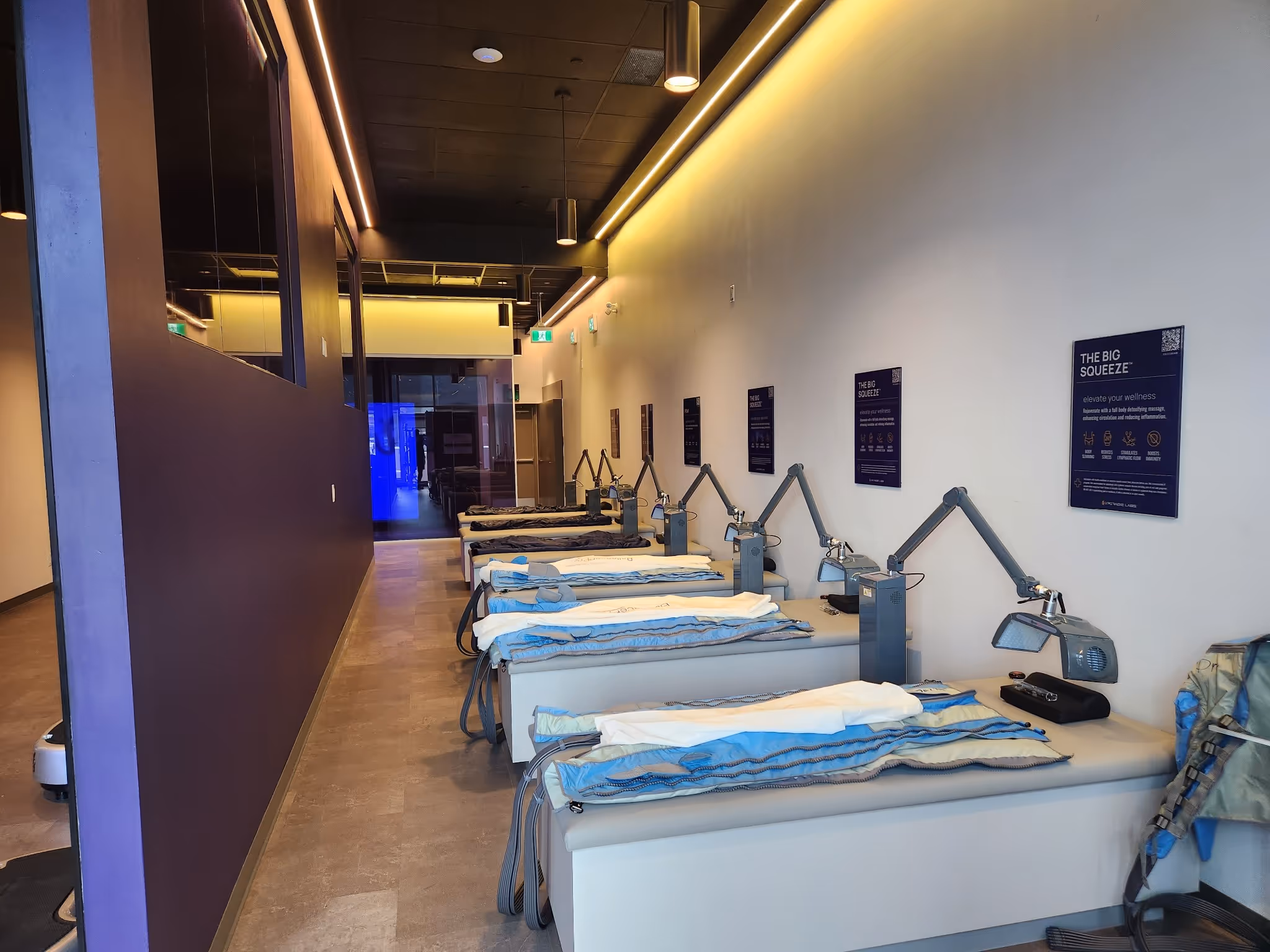 Row of therapy beds with attached adjustable lamps and informational posters on the wall in a wellness center.