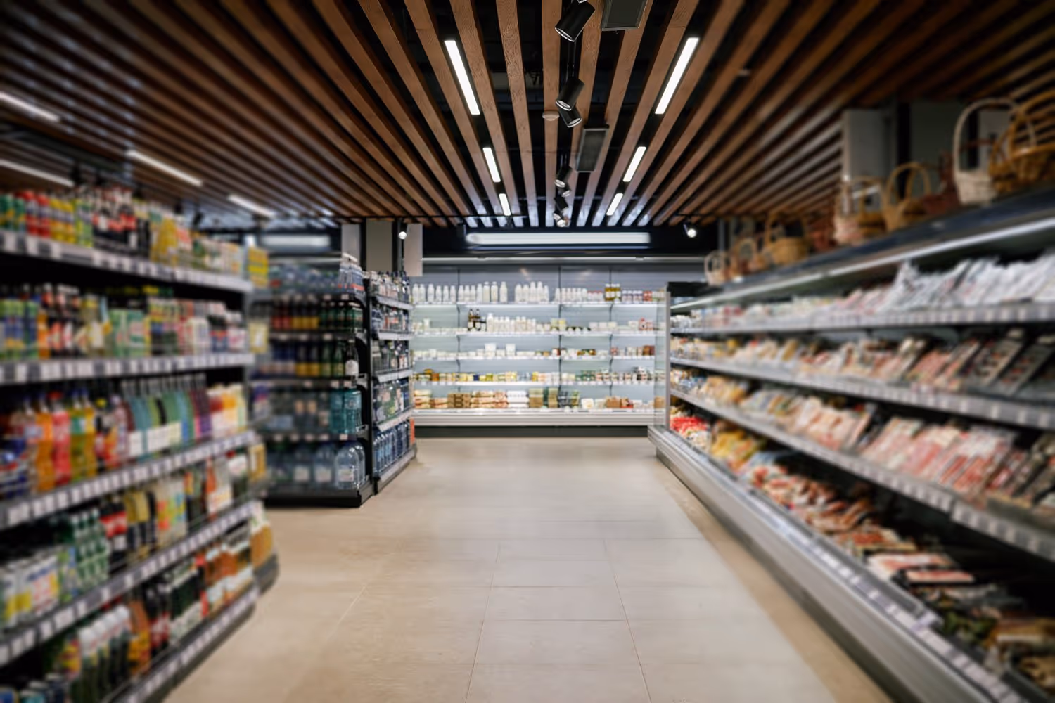 A supermarket aisle with shelves stocked on both sides, under a wooden slat ceiling with overhead lights.