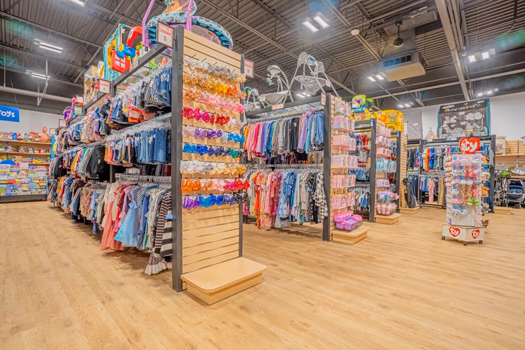 Interior view of a brightly lit children's clothing store with colorful outfits and accessories displayed on racks and shelves.