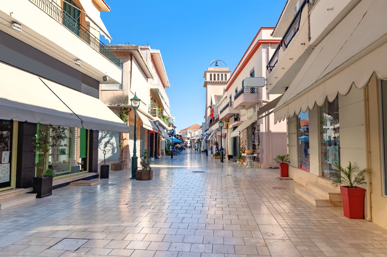 Sunlit pedestrian street lined with shops and buildings under a clear blue sky.