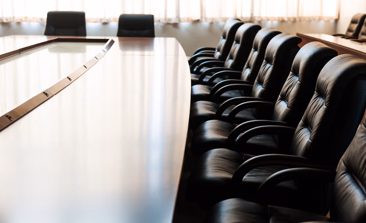 Row of black leather office chairs along a large polished conference table in a bright meeting room.