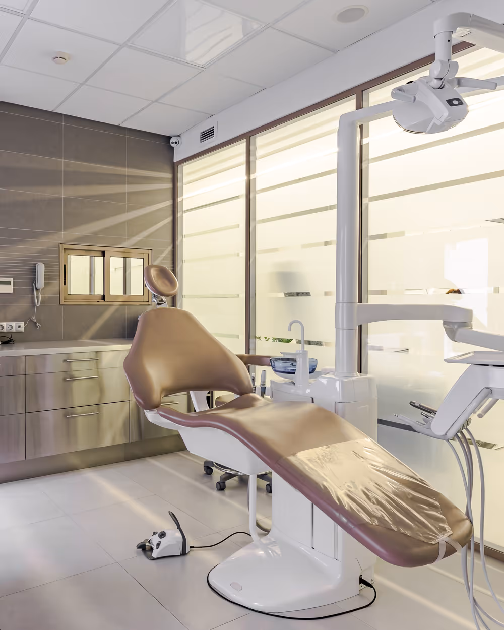 Modern dental office with a brown dental chair covered in plastic and dental equipment around it.