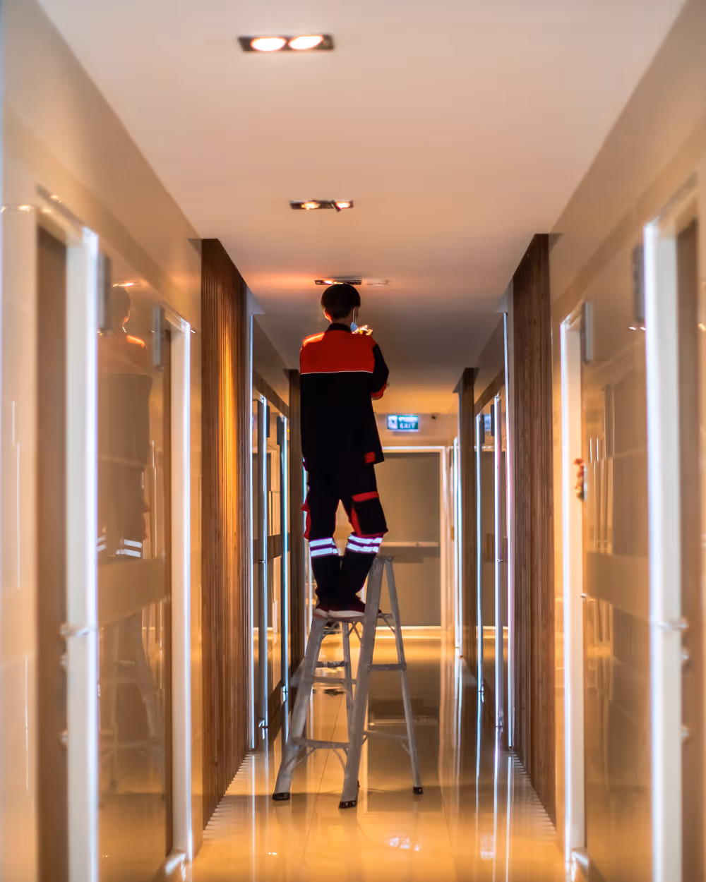 Person standing on a ladder in a hallway, performing maintenance on the ceiling light.