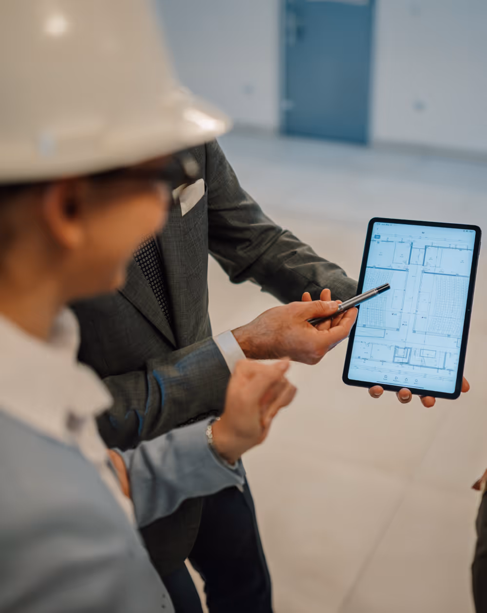 Two professionals reviewing architectural plans displayed on a tablet, with one person pointing at the screen with a pen.