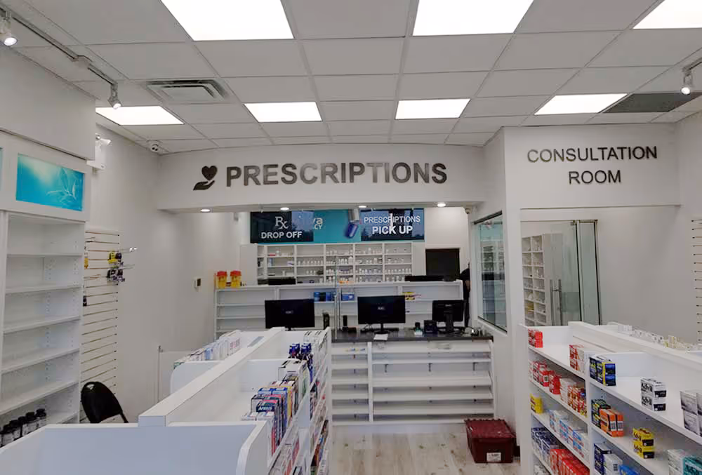 Interior of a bright pharmacy with signage for prescriptions and a consultation room, shelves with medication, and computer stations.