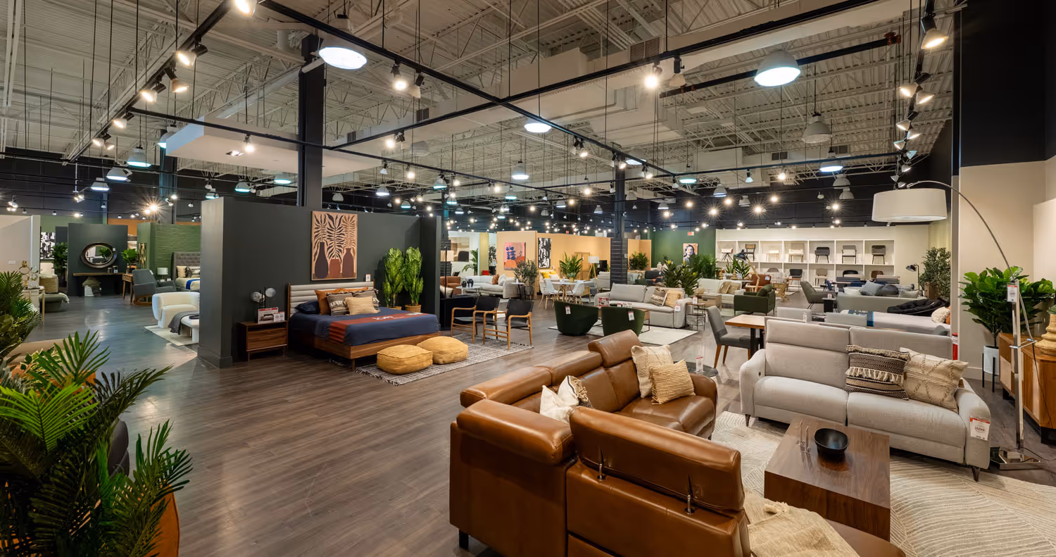 Spacious, well-lit furniture showroom displaying various sofas, beds, chairs, and decor arranged on wood flooring.
