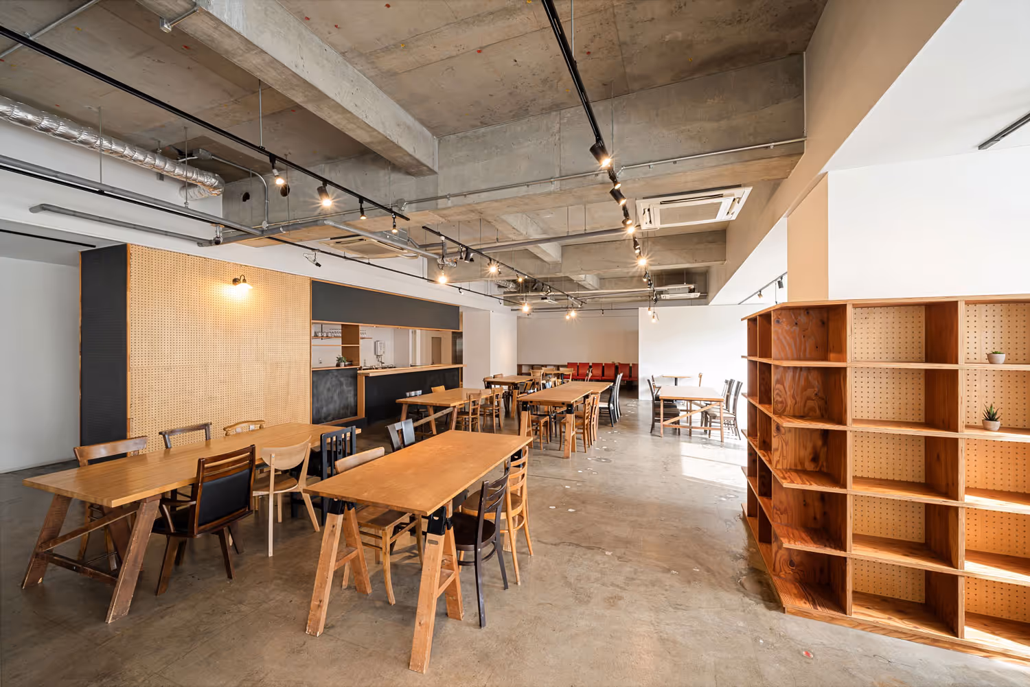 Spacious modern cafeteria with wooden tables and chairs, exposed concrete ceiling, and large empty wooden shelving unit.