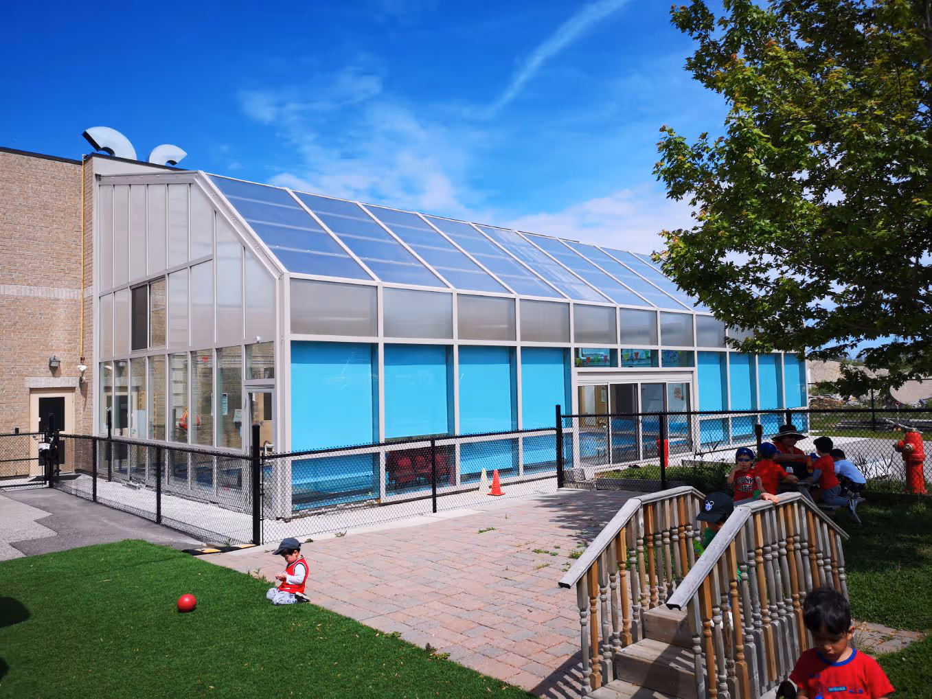 Children playing outside near a modern building with large glass windows and blue panels under a clear sky.
