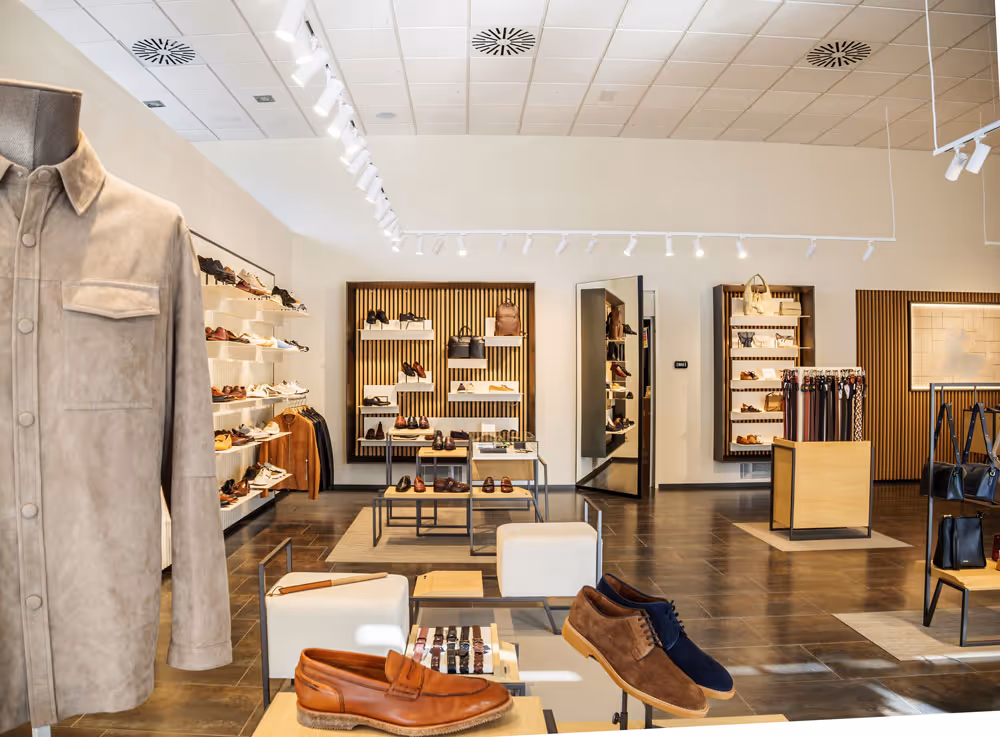 Interior of a modern shoe store with shelves of shoes, a mannequin wearing a beige jacket, and seating areas for customers.