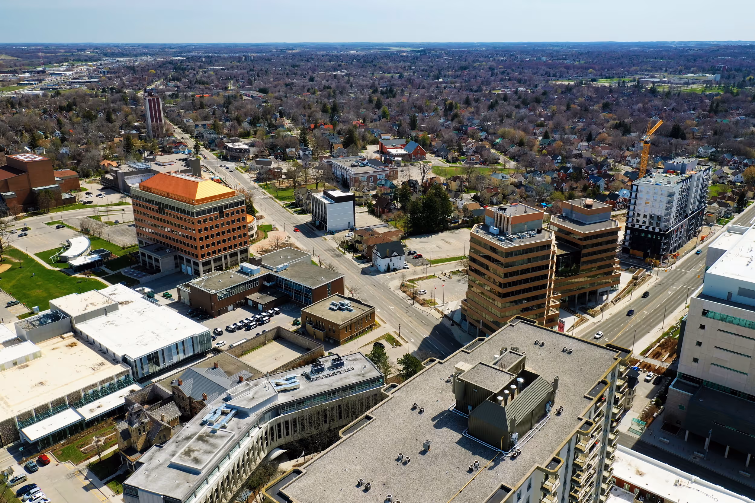 Aerial view of a cityscape with mid-rise office buildings, residential houses, and roads stretching into a distant horizon under a clear sky.