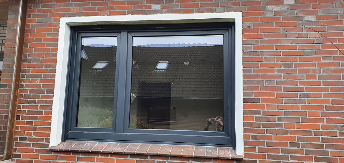 Modernes, zweiflügeliges Fenster mit schwarzem Rahmen in roter Backsteinwand.