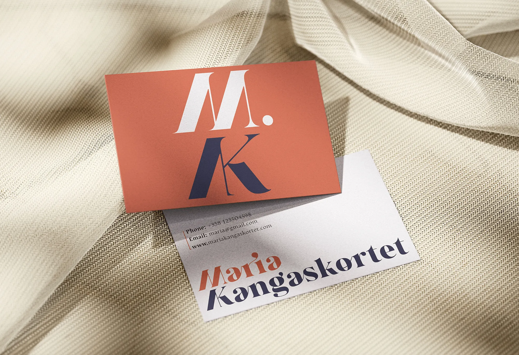 Two business cards on beige textured fabric, one with large stylized initials 'M.K.' and the other displaying contact info and the name Maria Kangaskortet.