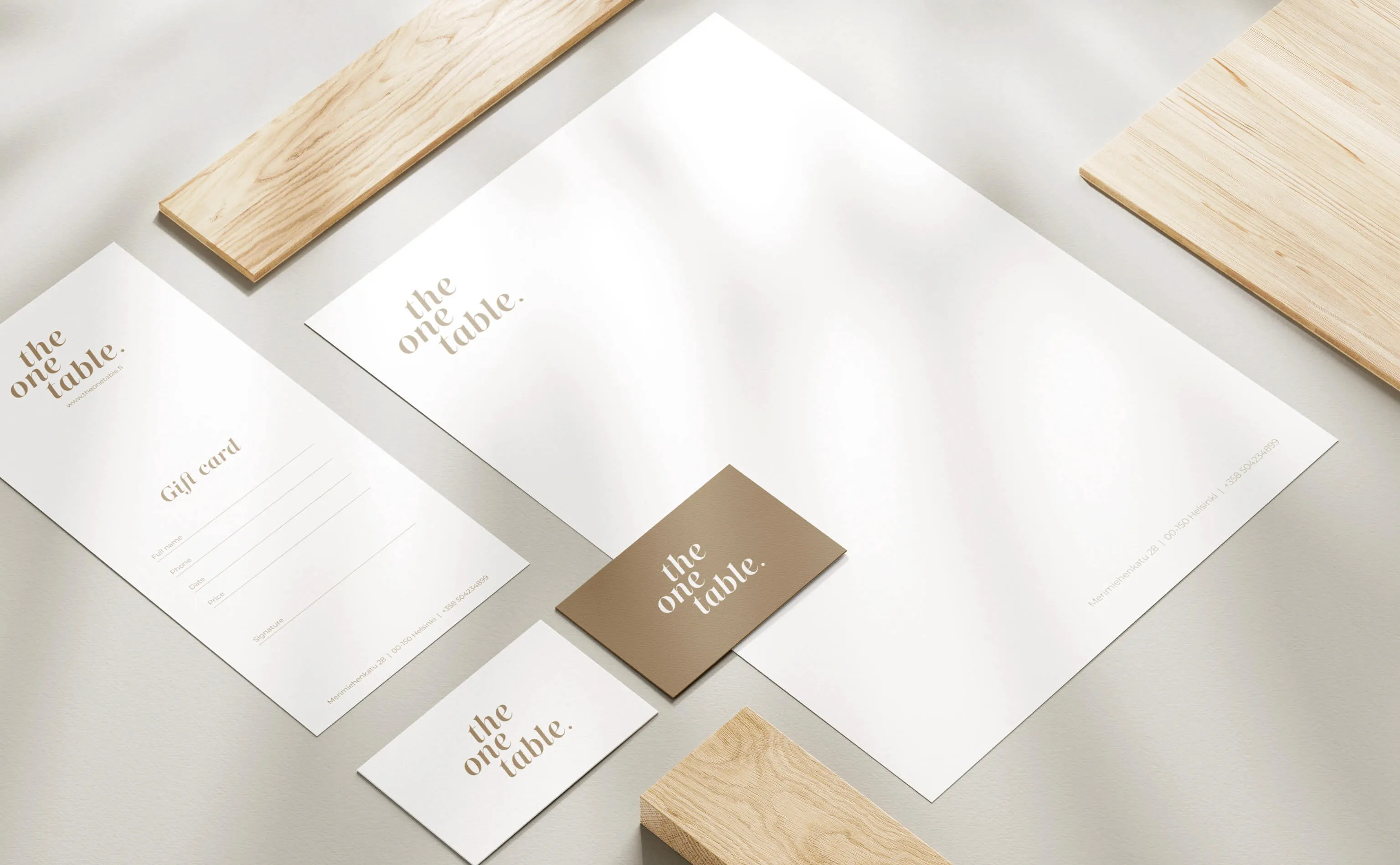 Minimalist branded stationery set for 'the one table' including a letterhead, gift card, and business cards on a light surface with wooden blocks.
